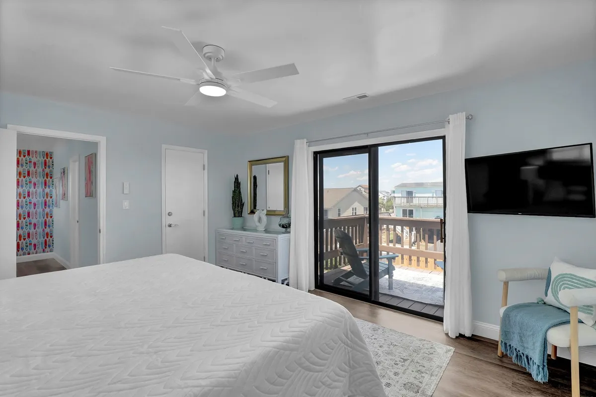 A cozy primary bedroom with a bed, dresser, television, and a sliding glass door that opens directly onto the deck. The connection to the outdoor space is visible, reinforcing the easy access described in the section.