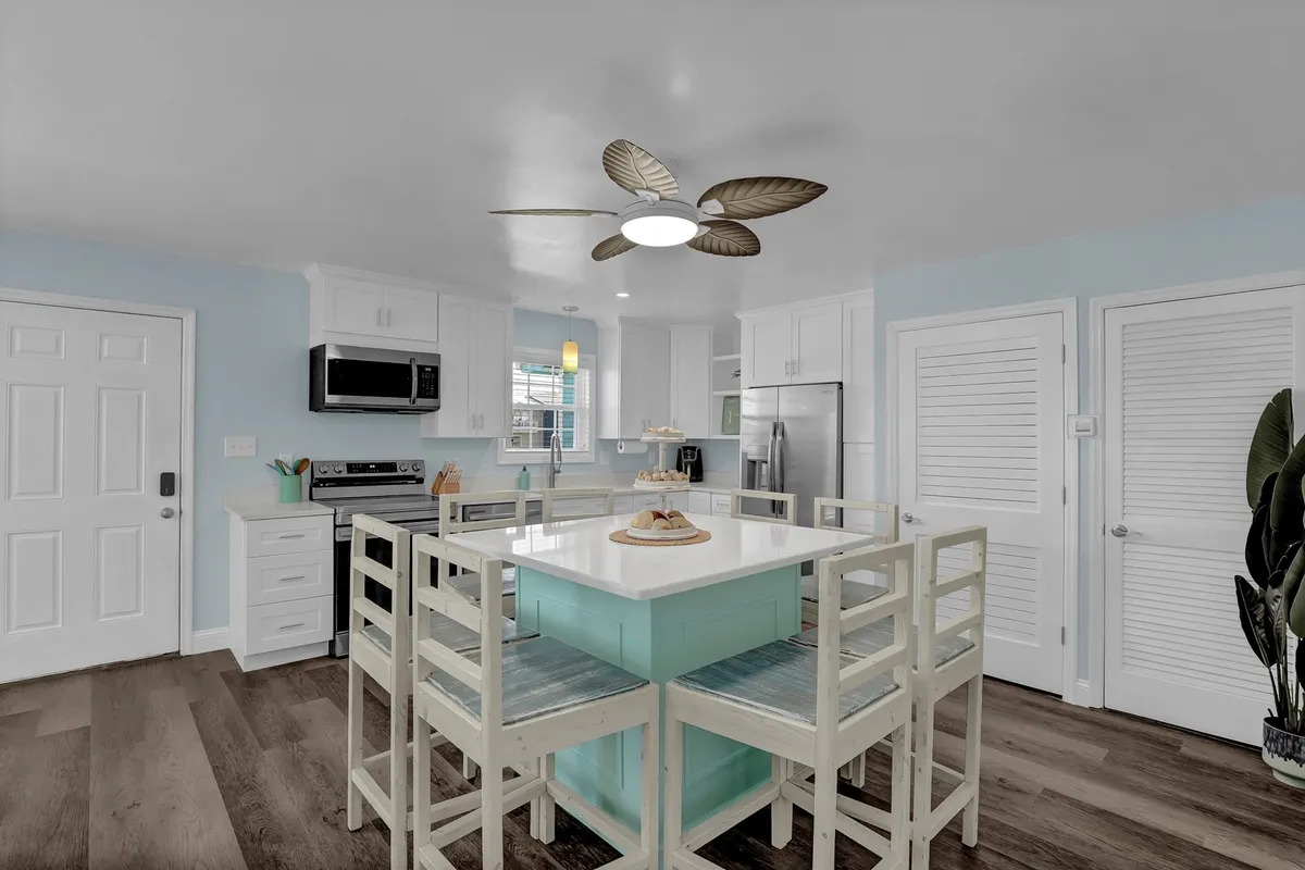 A bright, open kitchen featuring a central island, modern stainless steel appliances, and a decorative ceiling fan. The space is designed for both cooking and gathering, with ample prep space and a relaxed, cheerful atmosphere that invites conversation.