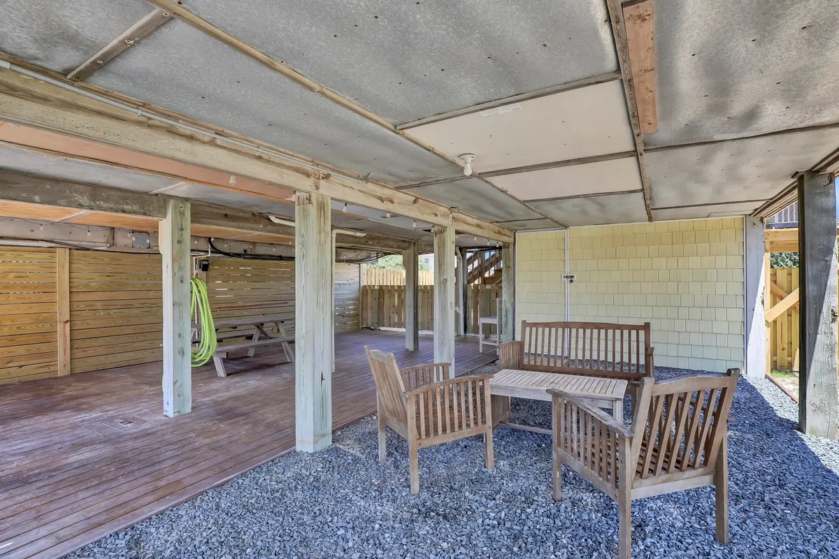 An outdoor area with wooden chairs and a table on gravel, shaded by supporting columns. This relaxed space is ideal for outdoor dining, social gatherings, or simply enjoying the coastal ambiance in an informal setting.