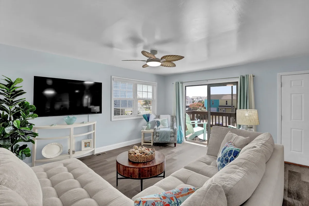 A cozy living room with a comfortable sofa, coffee table, and a television, complemented by a sliding glass door that allows natural light to flood the space. The decor is relaxed and inviting, with a view to the outdoors enhancing the sense of openness.