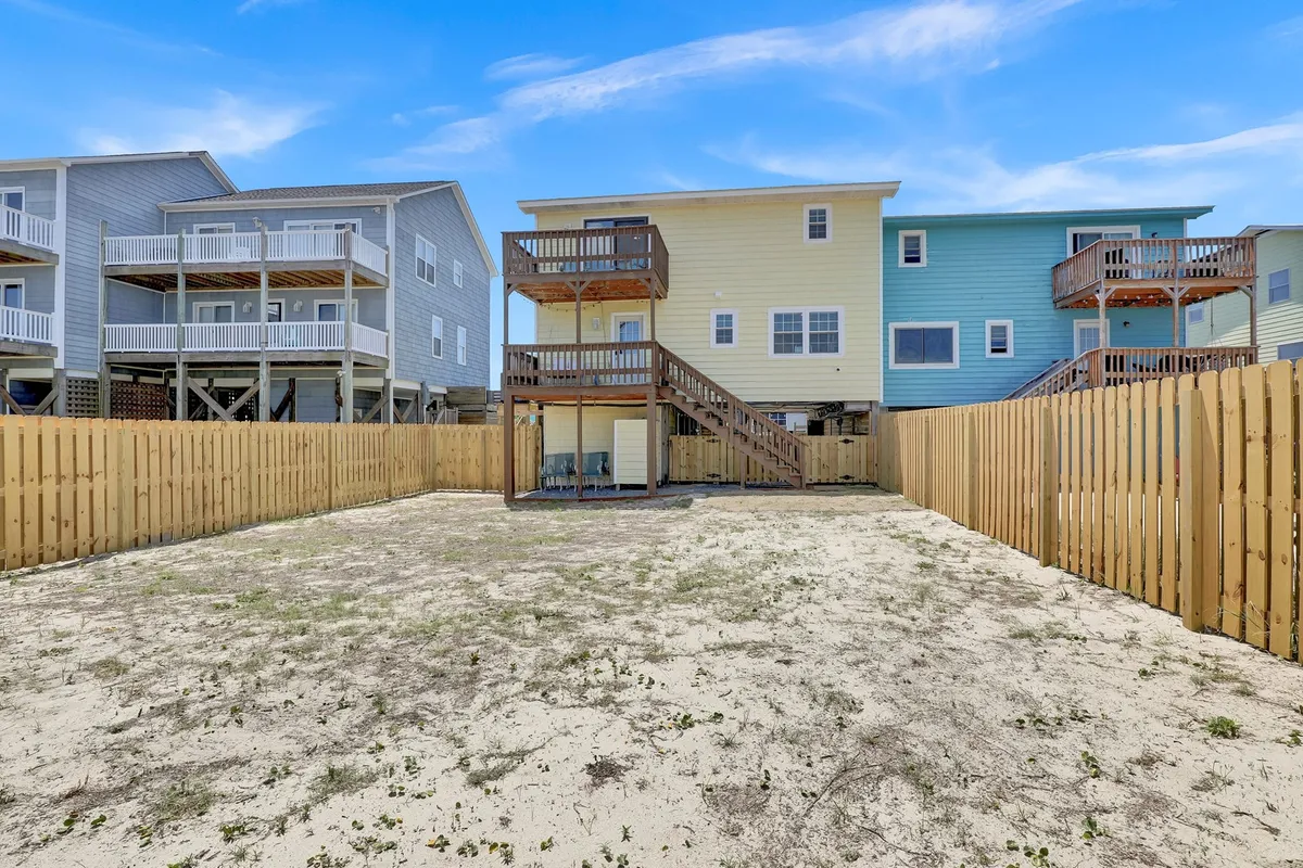 A casual and relaxed wooden deck area with a fenced yard, neighboring houses, and plenty of open space for barbecuing, playing games, or letting pets out for some fresh air. The setting is inviting and emphasizes outdoor living.