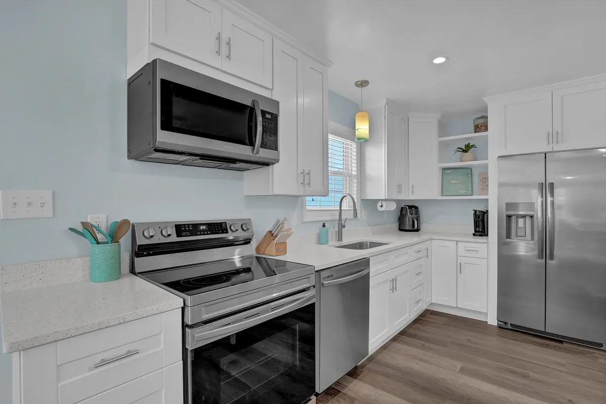 A crisp, inviting kitchen with gleaming stainless steel appliances, white cabinetry, light blue walls, and spacious countertops. The design feels functional yet homey, ideal for preparing everything from simple breakfasts to festive seafood feasts.