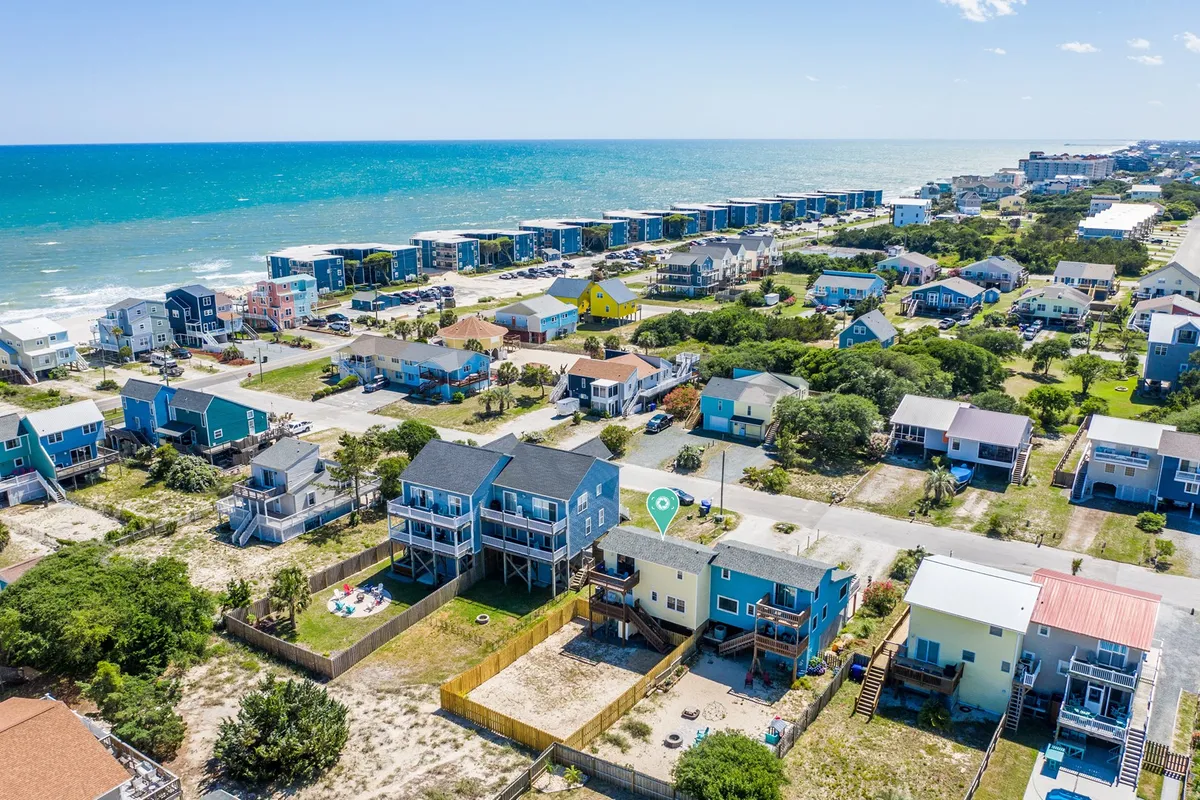 A cheerful view featuring colorful houses with ocean views, a backyard area, a swimming pool, and clear proximity to the beach. The inviting layout showcases the close relationship between the property and the shore, emphasizing easy access to beach adventures.